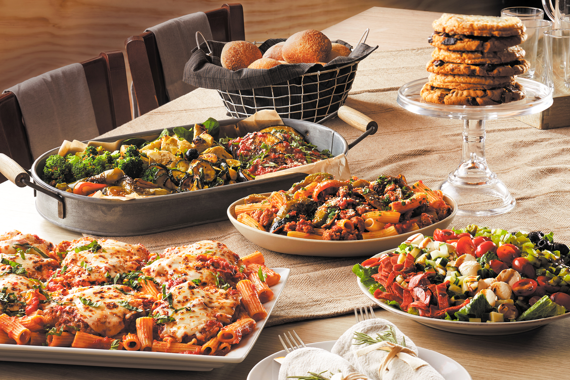 Trays of pasta, chicken, and cookies catered from Bertucci's on a dining room table.