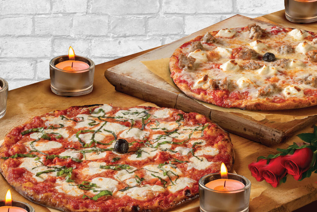 Two Bertucci's pizzas on a table with candles and roses