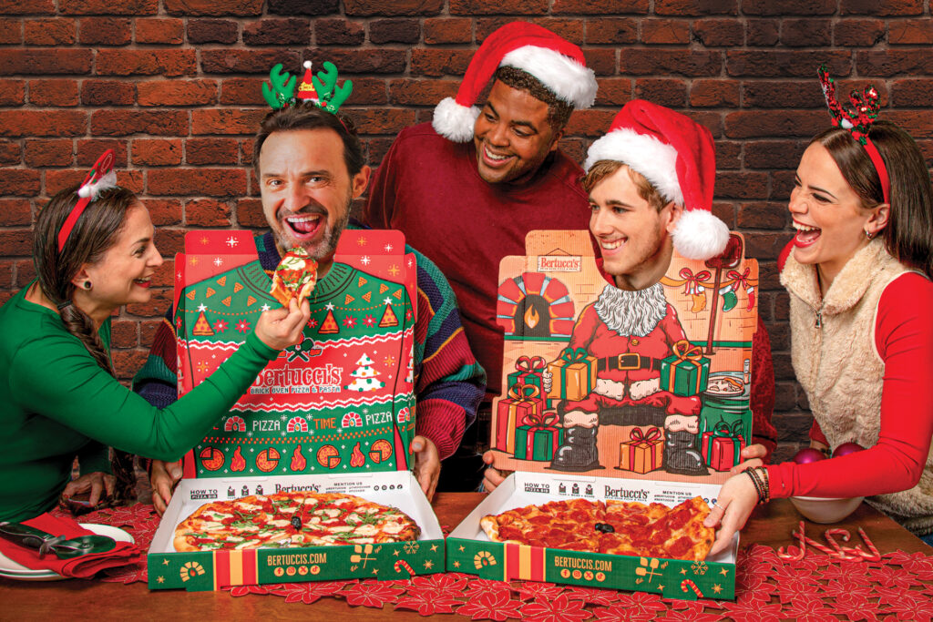 A group of friends posing with the holiday-printed pizza boxes