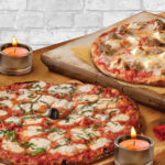 Two Bertucci's pizzas on a table with candles and roses