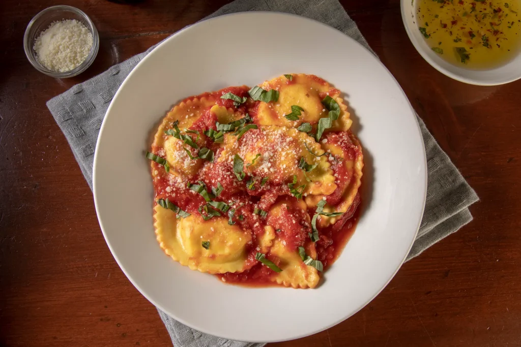 Four-cheese ravioli topped with tomato sauce, grated cheese, and fresh basil.