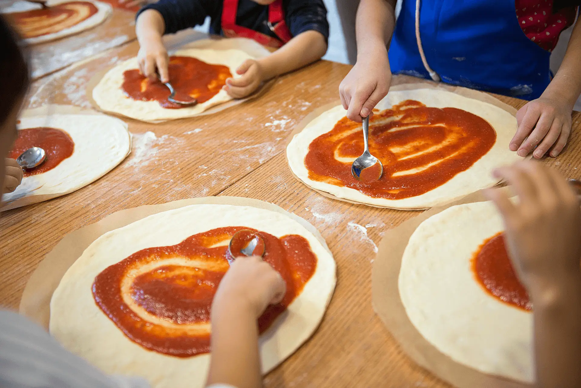 Bertucci's Little Chefs Party kids spreading pizza sauce on raw dough